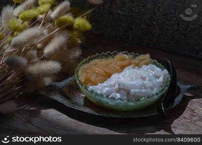 Kanom pla krim khai tao or Sweet rice noodles with coconut cream in glass bowl served with black spoon. Traditional thai dessert, Copy space, Selective focus.