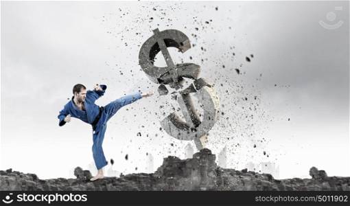 Karate man attack dollar. Young determined karate man breaking with leg concrete dollar sign