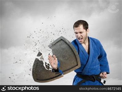 Karate man in blue kimino. Young determined karate man breaking concrete shield