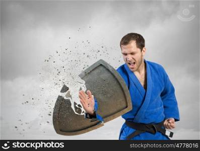 Karate man in blue kimino. Young determined karate man breaking concrete shield