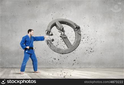 Karate man in blue kimino. Young determined karate man breaking concrete stop sign