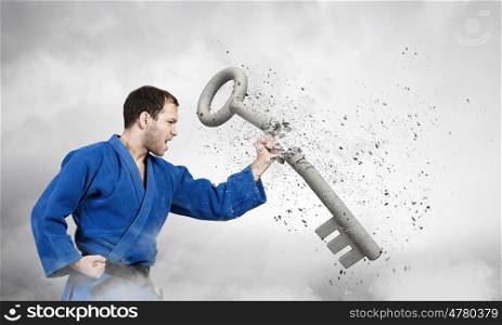 Karate man in blue kimino. Young determined karate man breaking with anger concrete key