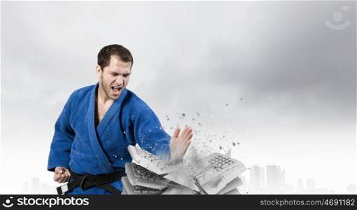 Karate man in blue kimino. Young determined karate man breaking with hand concrete bricks