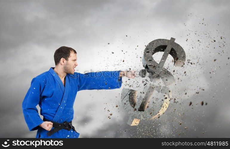 Karate man in blue kimino. Young determined karate man breaking with hand concrete dollar sign