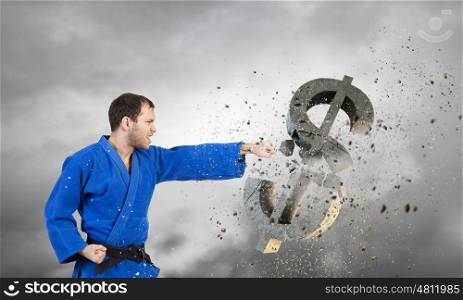 Karate man in blue kimino. Young determined karate man breaking with hand concrete dollar sign