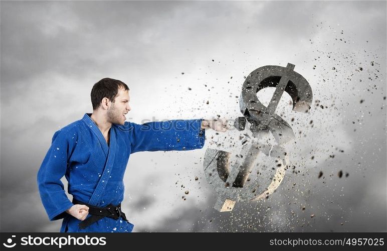 Karate man in blue kimino. Young determined karate man breaking with hand concrete dollar sign