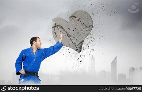 Karate man in blue kimino. Young determined karate man breaking with hand concrete heart