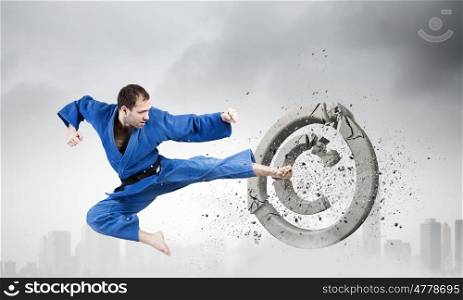 Karate man in blue kimino. Young determined karate man breaking with leg concrete copyright sign