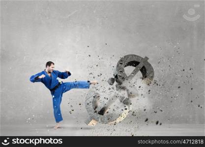 Karate man in blue kimino. Young determined karate man breaking with leg concrete dollar sign