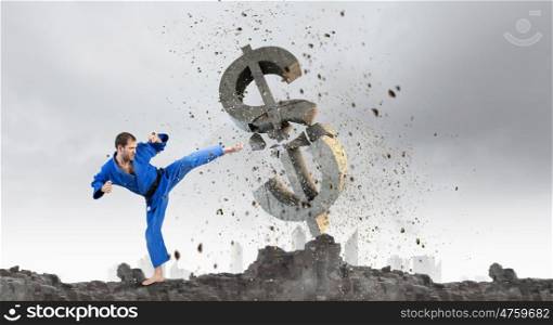 Karate man in blue kimino. Young determined karate man breaking with leg concrete dollar sign