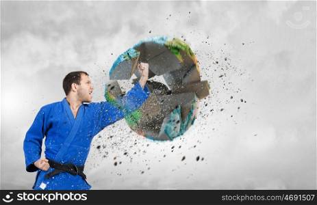 Karate man in blue kimino. Young determined karate man breaking with leg concrete Earth planet. Elements of this image are furnished by NASA