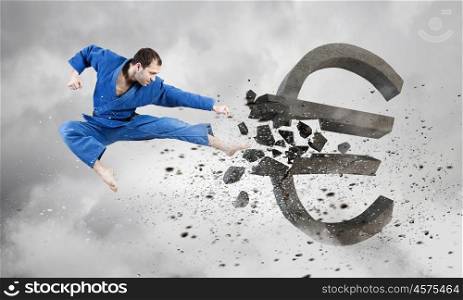 Karate man in blue kimino. Young determined karate man breaking with leg concrete euro sign