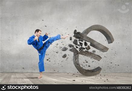 Karate man in blue kimino. Young determined karate man breaking with leg concrete euro sign