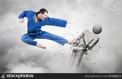 Karate man in blue kimino. Young determined karate man breaking with leg concrete figure