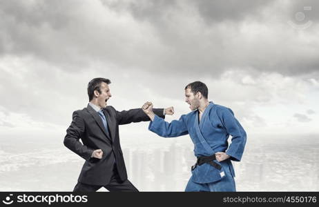 Karate man in blue kimino. Young determined karate man fighting with businessman in suit