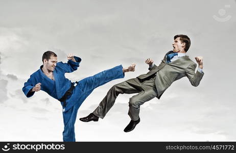 Karate man in blue kimino. Young determined karate man fighting with businessman in suit