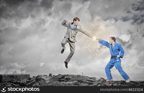 Karate man in blue kimino. Young determined karate man fighting with businessman in suit