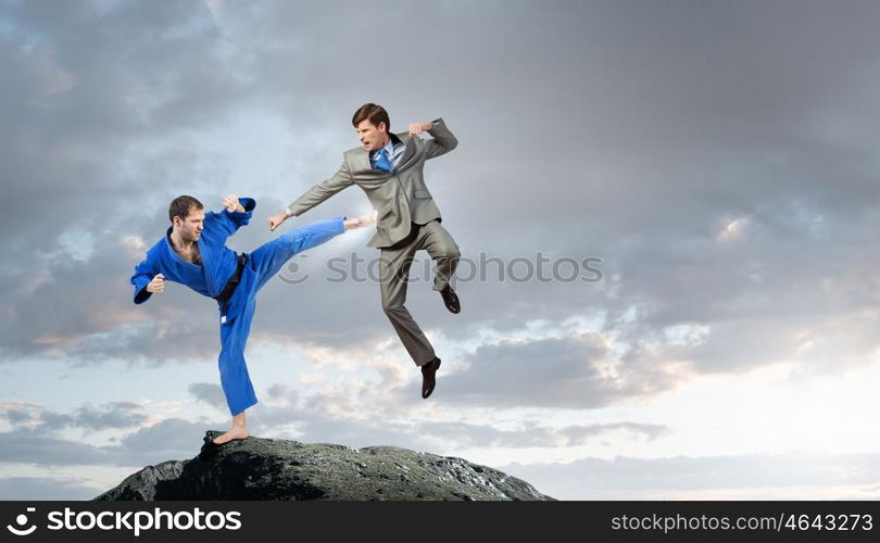 Karate man in blue kimino. Young determined karate man fighting with businessman in suit