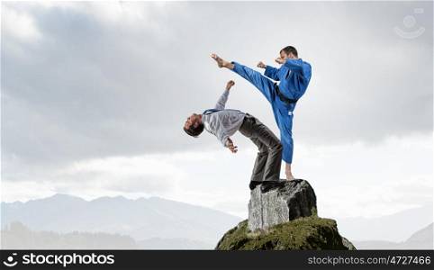 Karate man in blue kimino. Young determined karate man fighting with businessman in suit