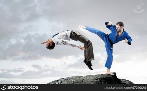 Karate man in blue kimino. Young determined karate man fighting with businessman in suit