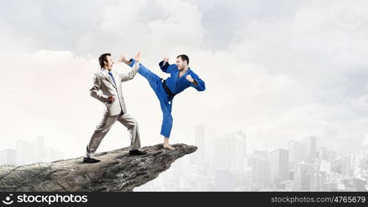 Karate man in blue kimino. Young determined karate man fighting with businessman in suit