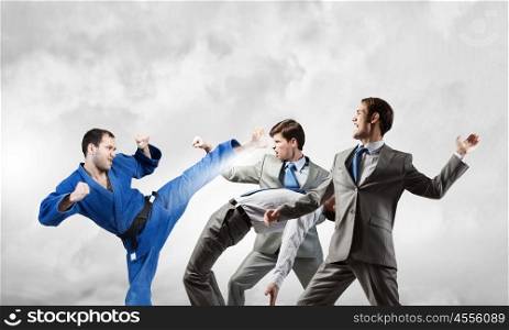 Karate man in blue kimino. Young determined karate man fighting with team of businesspeople