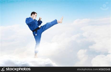 Karate man in blue kimino. Young determined karate man on cloud high in sky