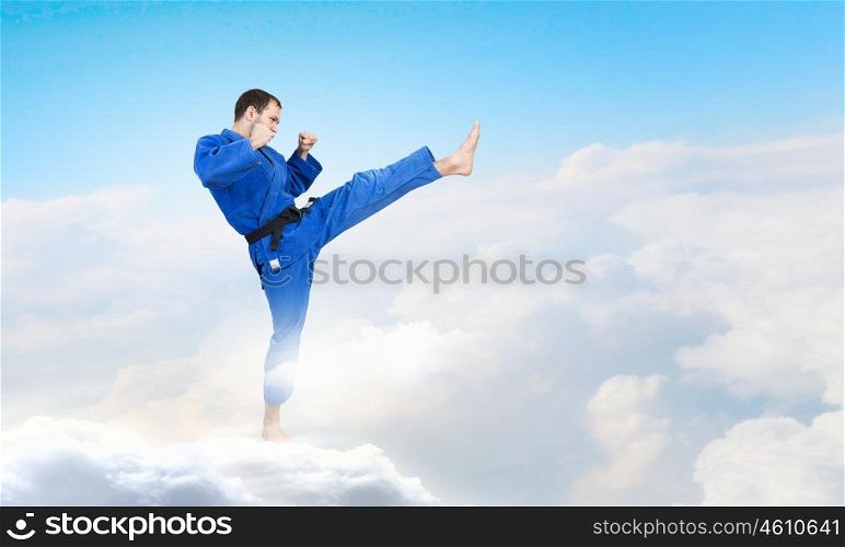 Karate man in blue kimino. Young determined karate man on cloud high in sky