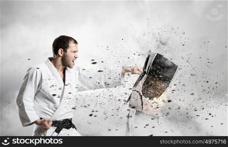 Karate man in white kimino. Young determined karate man breaking personal computer