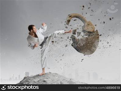 Karate man in white kimino. Young determined karate man breaking with anger concrete lock
