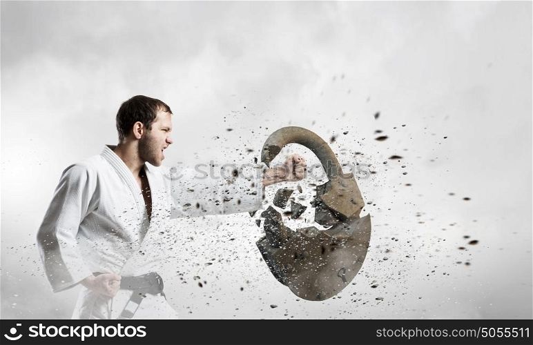 Karate man in white kimino. Young determined karate man breaking with anger concrete lock