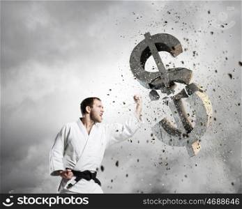 Karate man in white kimino. Young determined karate man breaking with hand concrete dollar sign