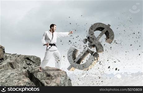 Karate man in white kimino. Young determined karate man breaking with hand concrete dollar sign
