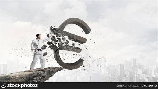 Karate man in white kimino. Young determined karate man breaking with hand concrete euro sign