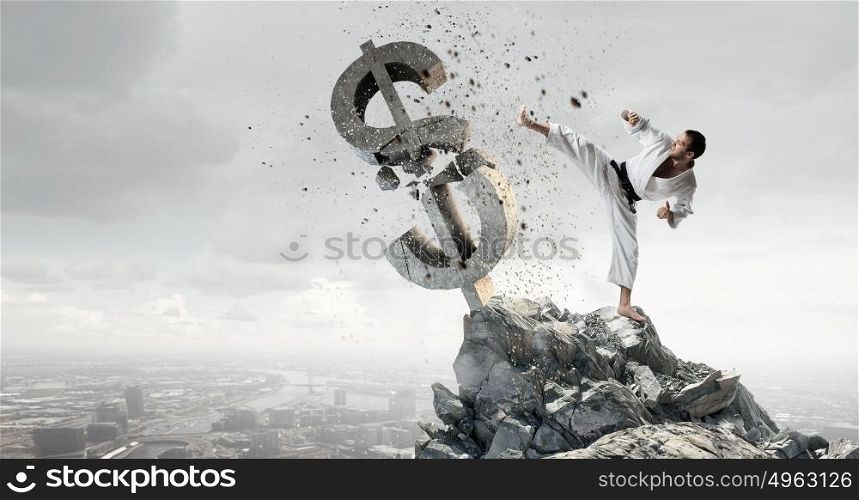Karate man in white kimino. Young determined karate man breaking with leg concrete dollar sign