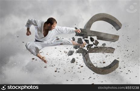 Karate man in white kimino. Young determined karate man breaking with leg concrete euro sign