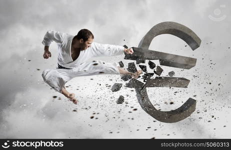 Karate man in white kimino. Young determined karate man breaking with leg concrete euro sign