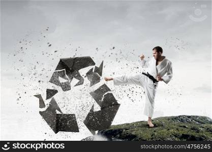 Karate man in white kimino. Young determined karate man breaking with leg concrete recycle sign