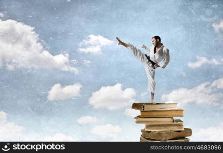 Karate man in white kimino. Young determined karate man on pile of books