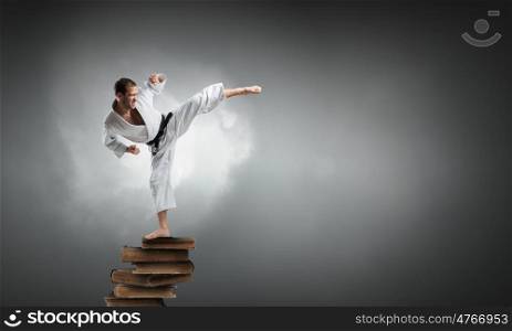 Karate man in white kimino. Young determined karate man on pile of books