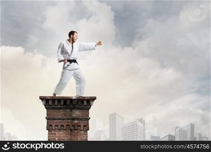 Karate man in white kimino. Young determined karate man on top high in sky