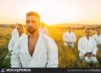 Karate master on training with his group, summer field on background. Martial art school on workout outdoor, technique practice