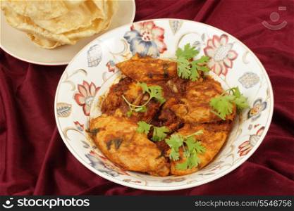 Kashmiri chicken in a serving bowl beside a plate of pappadums