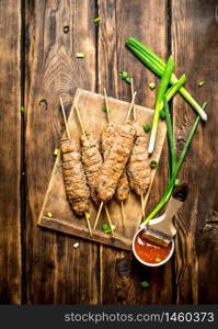 Kebab with green onions and hot sauce. On a wooden table.. Kebab with green onions and hot sauce.