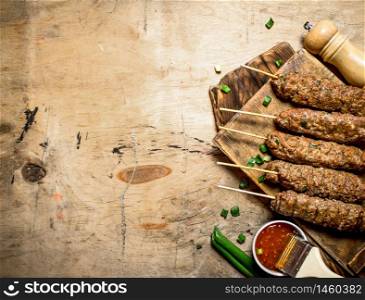 Kebab with green onions and hot sauce. On a wooden table.. Kebab with green onions and hot sauce.