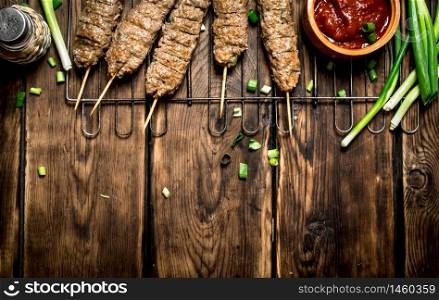 Kebab with tomato sauce and green onions. On a wooden table.. Kebab with tomato sauce and green onions.