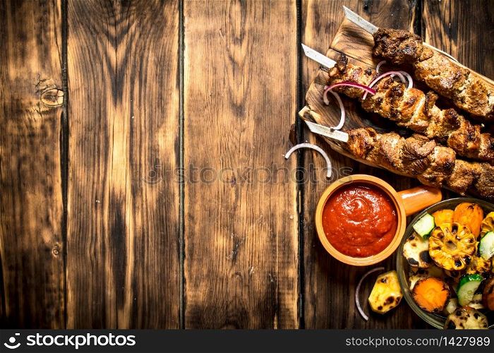 Kebab with tomato sauce and roasted vegetables. On wooden background.. Kebab with tomato sauce and roasted vegetables.