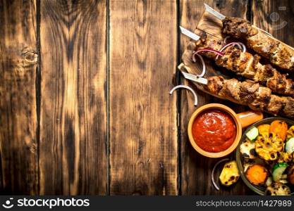 Kebab with tomato sauce and roasted vegetables. On wooden background.. Kebab with tomato sauce and roasted vegetables.