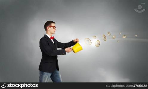 Keep your investments safe. Young businessman holding bucket with coins flying out