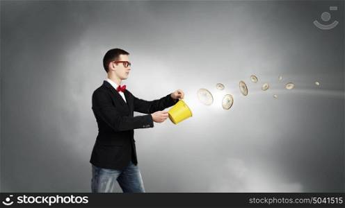 Keep your investments safe. Young businessman holding bucket with coins flying out